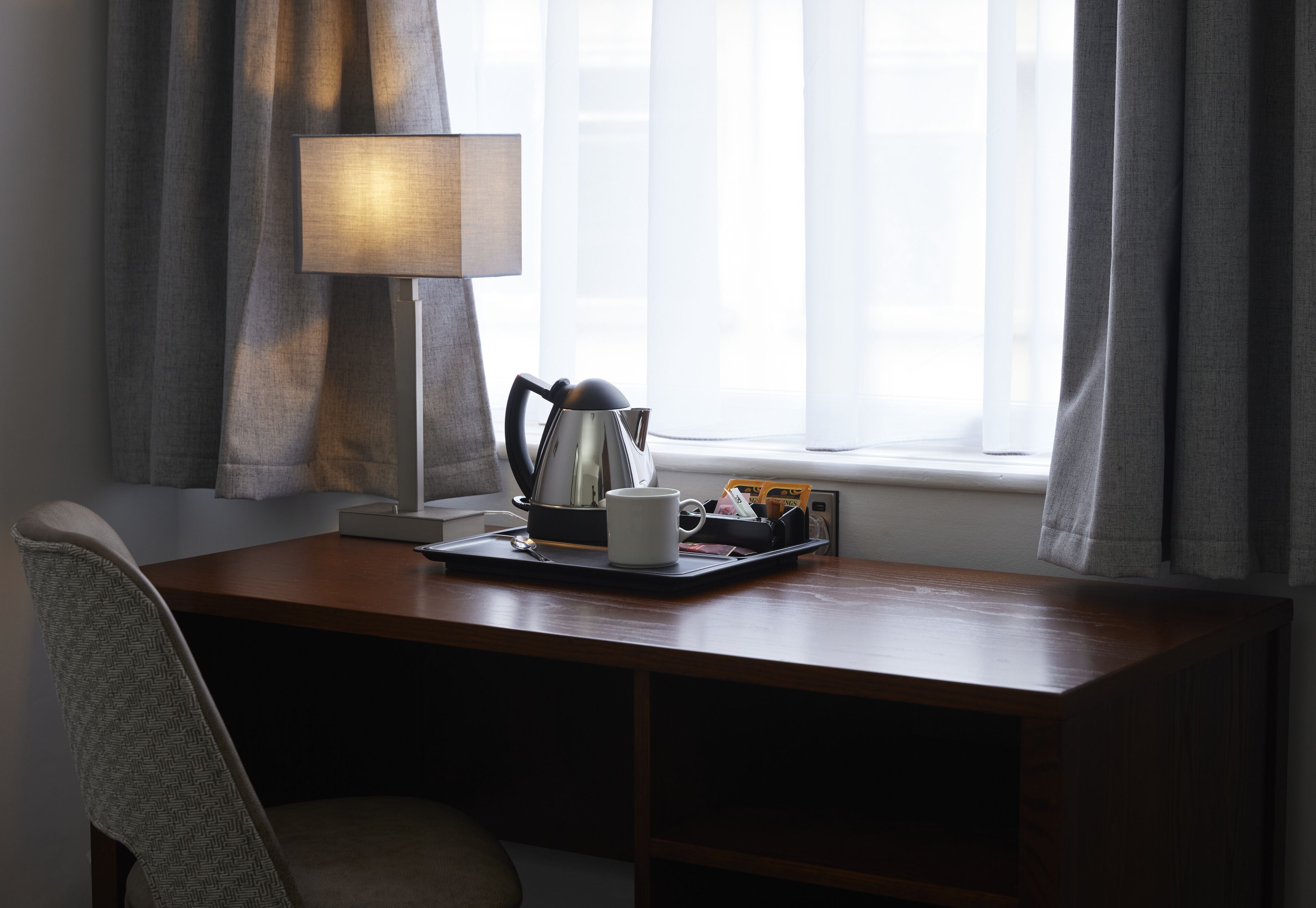 A wooden desk with a lamp, a mug, and a tray with a teapot and cups.
