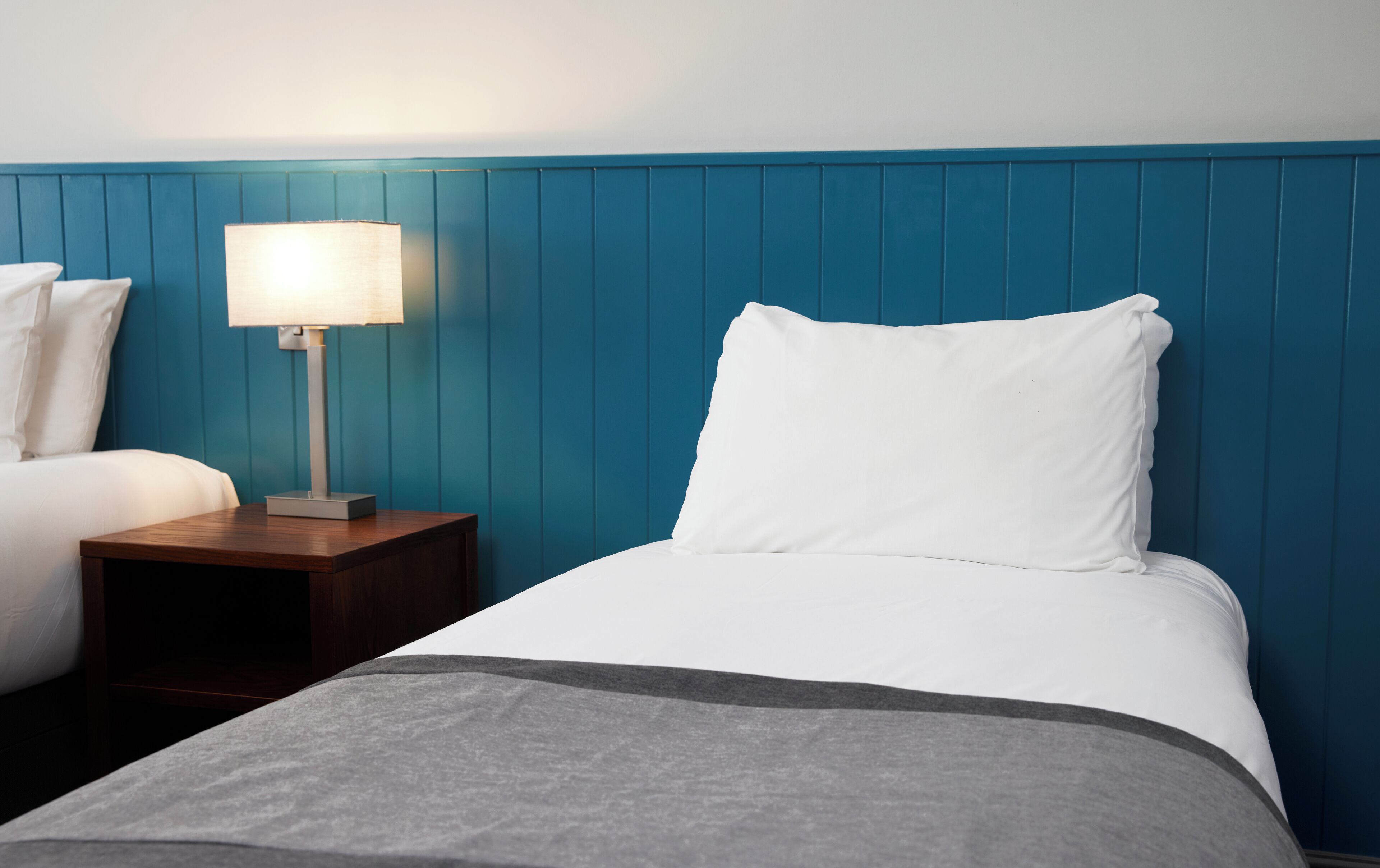 Una habitación de hotel con una cama, una mesita de noche, una lámpara y una pared azul.