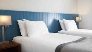 Dos camas individuales con sábanas y almohadas blancas, un cabecero azul y lámparas de noche.