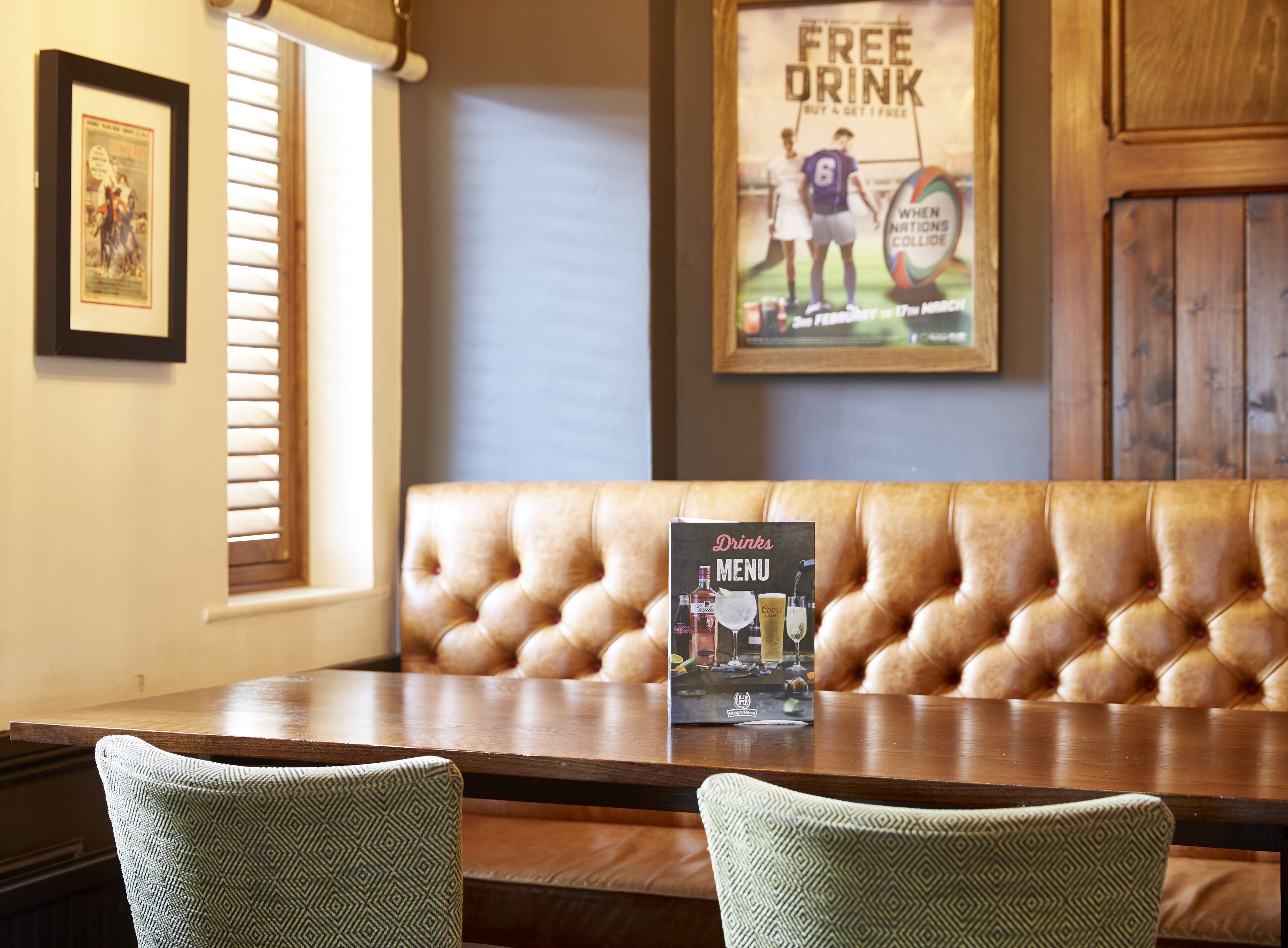 A restaurant interior with a wooden table, cushioned bench, framed pictures, and a menu sign.