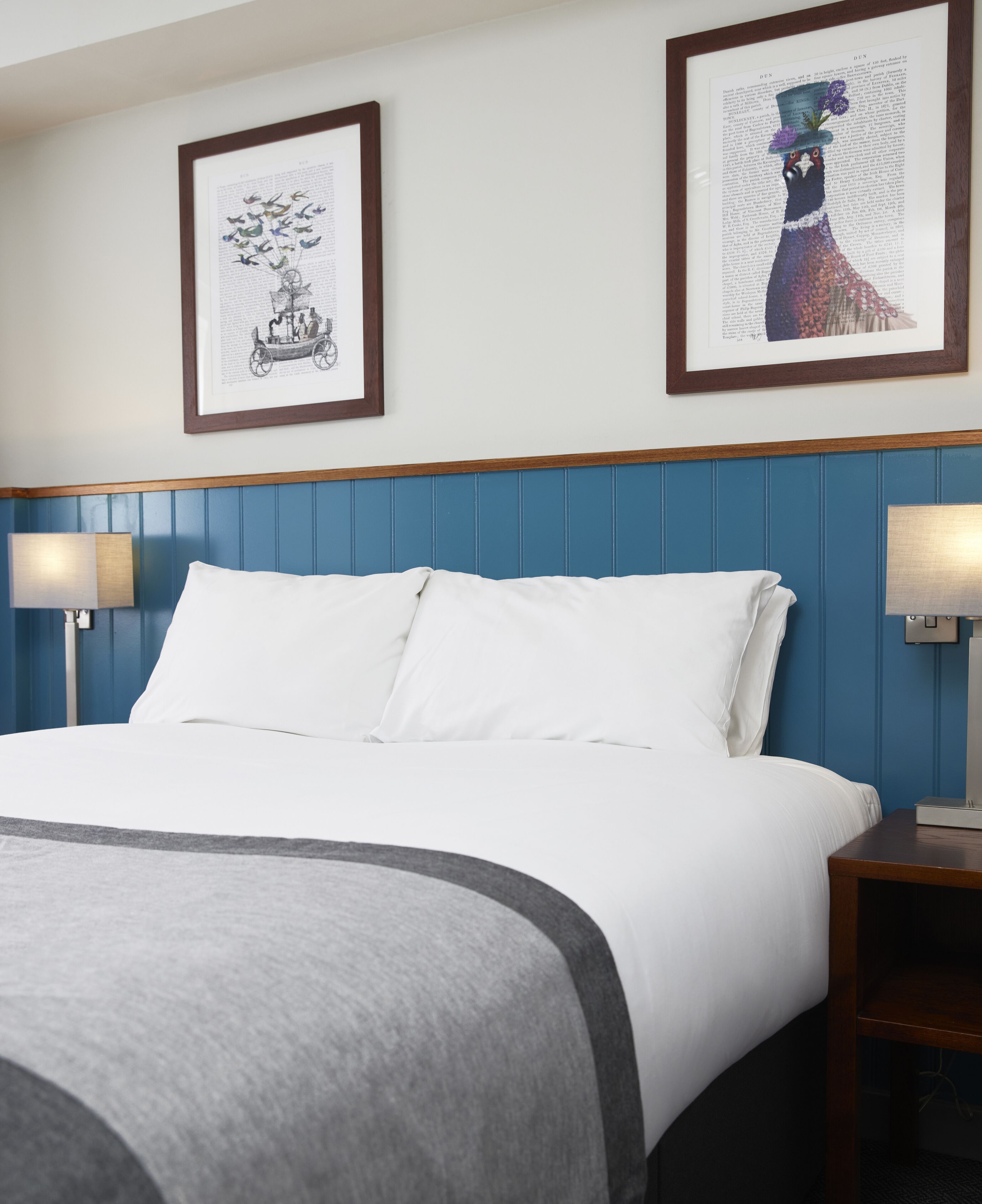 Cama bem arrumada com lençóis brancos, cabeceira azul e duas luminárias de cabeceira.