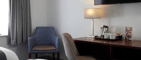 Habitación de hotel con cama, escritorio con lámpara, silla, televisor y ventana con cortinas.