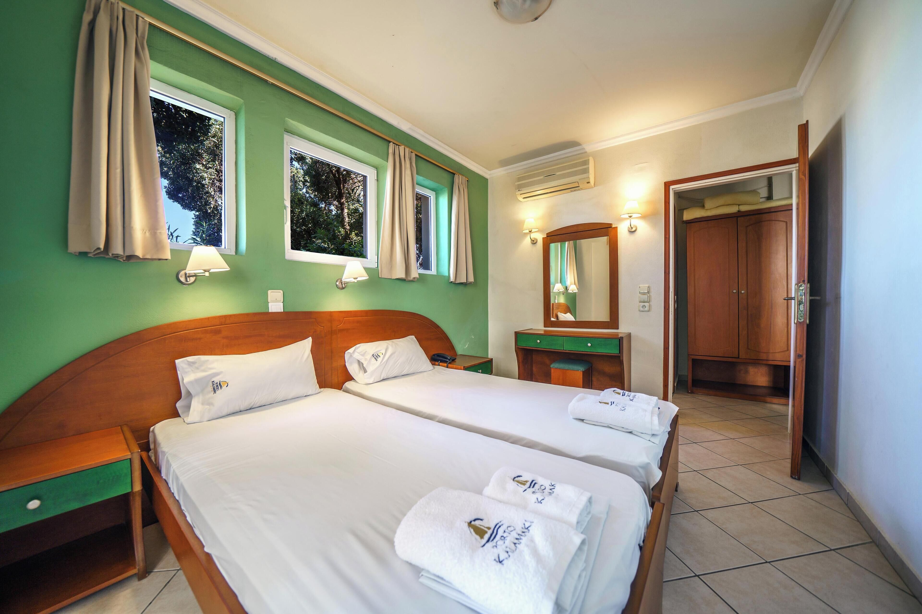 A hotel room with two beds, a wooden headboard, a nightstand, a mirror, and a wardrobe.