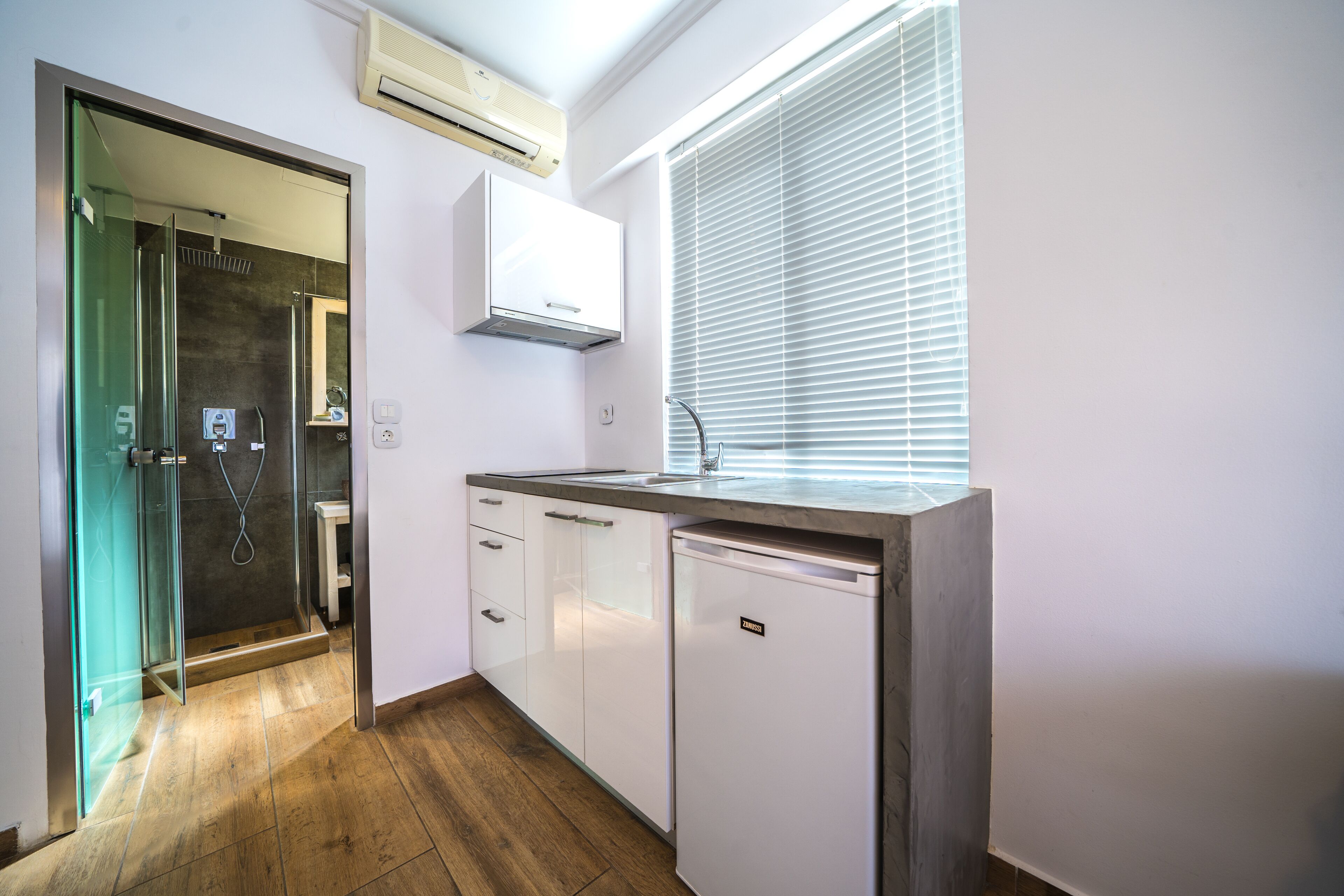 A compact kitchen with white cabinets, a built-in dishwasher, and a window with blinds.