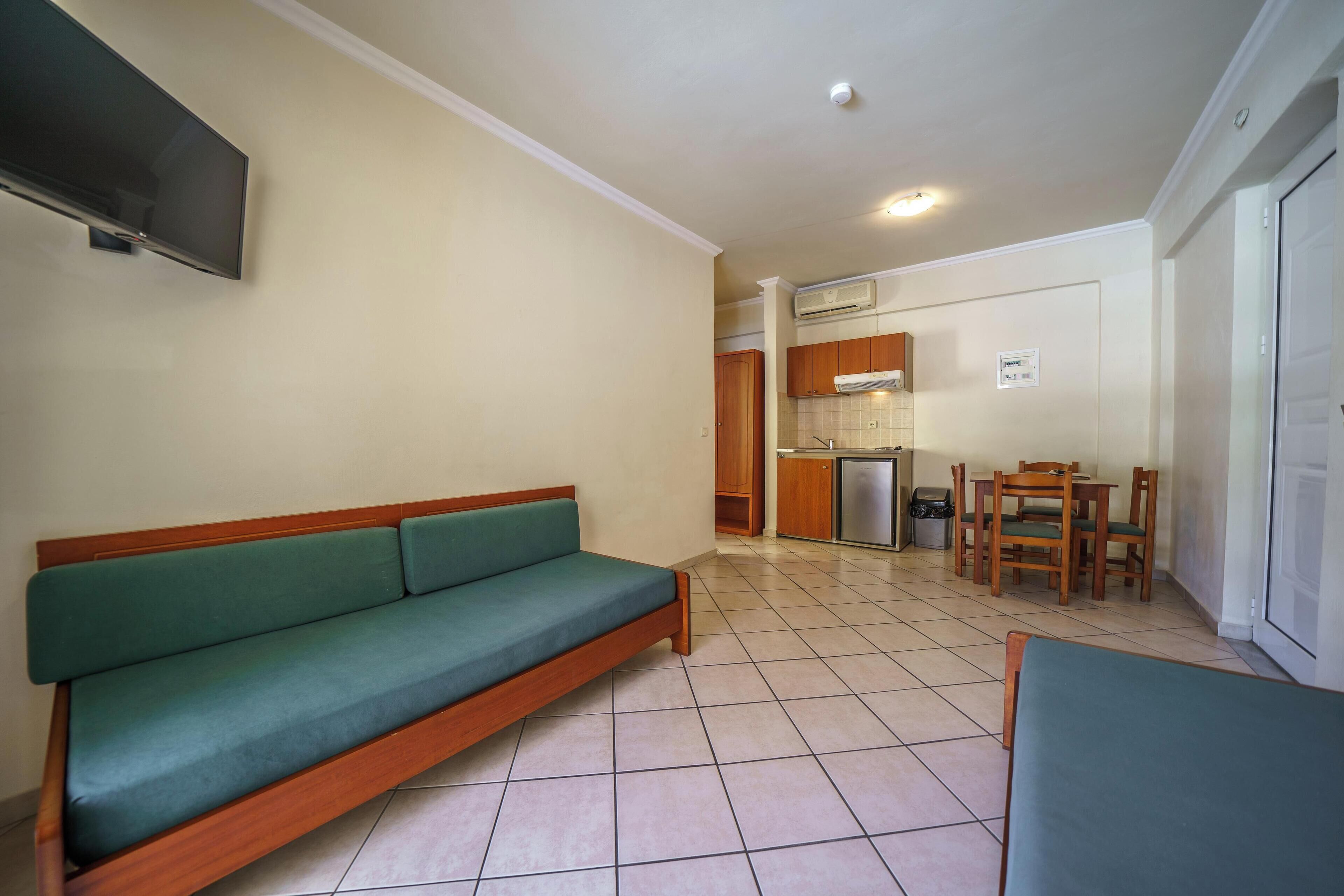 Un espacio habitable compacto con sofá, mesa de comedor, sillas, televisor y kitchenette.