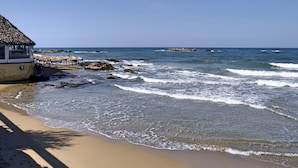 A beach with a thatched-roof hut and a rocky shoreline. - Porto Kalamaki Hotel (Chania)