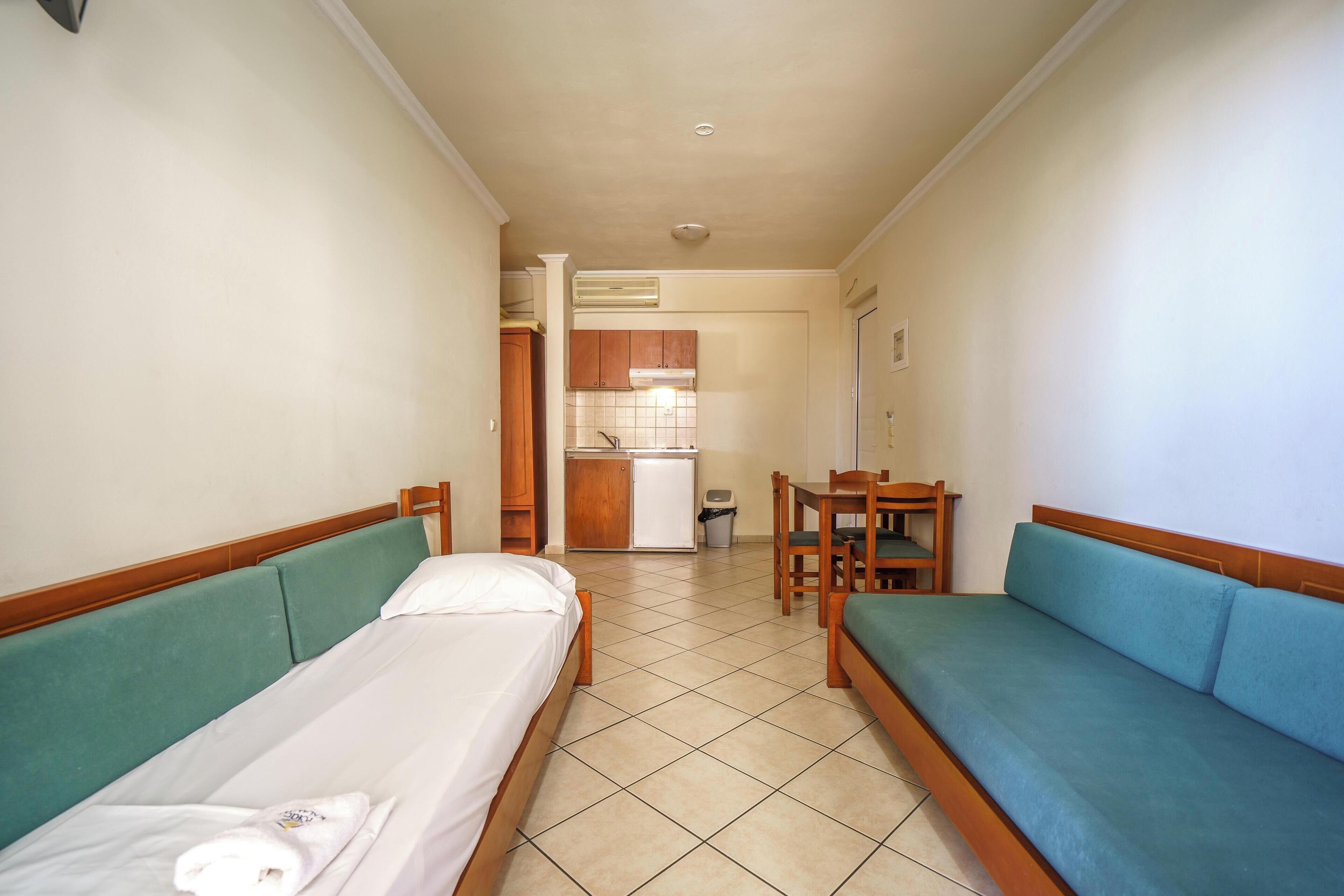 A hotel room with a bed, a sofa, a small table, and a kitchenette in the background.
