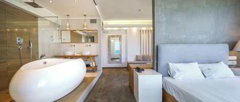 A modern hotel room with a large bathtub, a wooden vanity, a bed with white linens, and a large mirror.