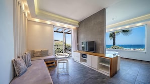 A modern living room with a sofa, TV, and a balcony with a view of the sea. - Porto Kalamaki Hotel (Chania)