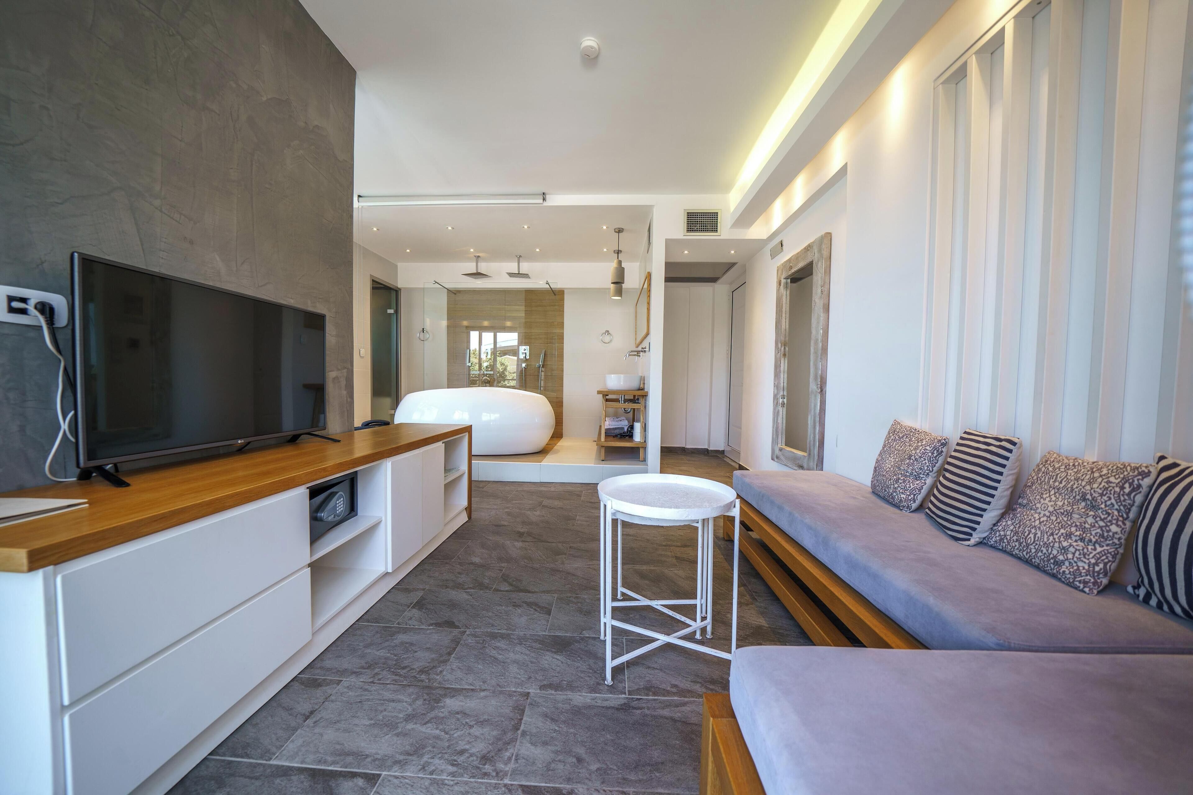 Una sala de estar moderna con un televisor de pantalla plana, un mueble bajo de madera, un sofá gris y un taburete blanco pequeño.