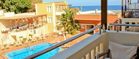 A balcony with a pool, lounge chairs, and a view of the sea.