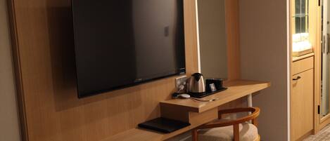 A hotel room with a wooden desk, a flat-screen TV, a small coffee maker, a laptop, and a chair.