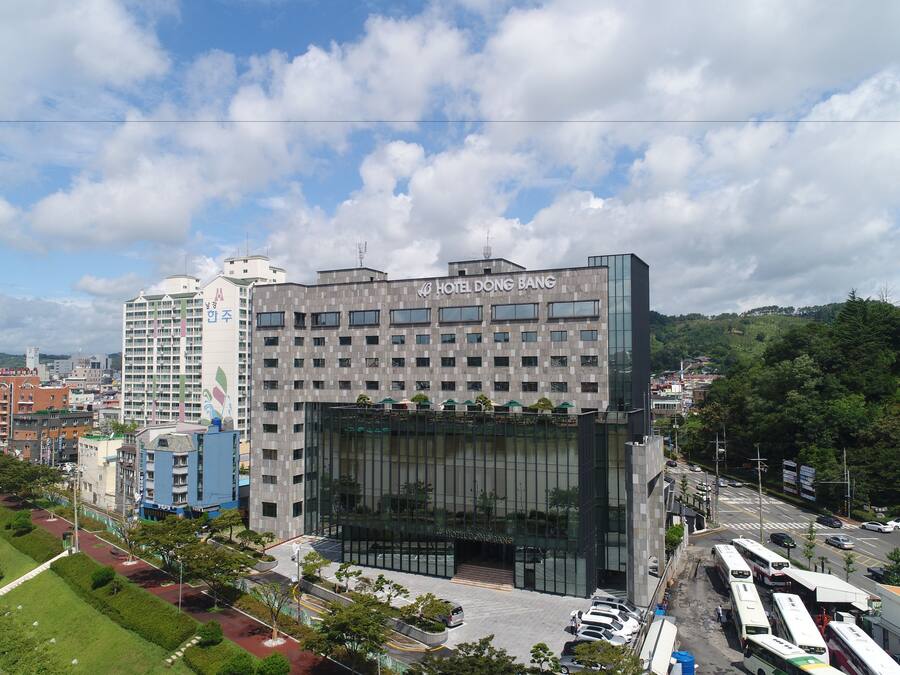 A modern hotel with a glass facade, multiple floors, and a parking area with buses.