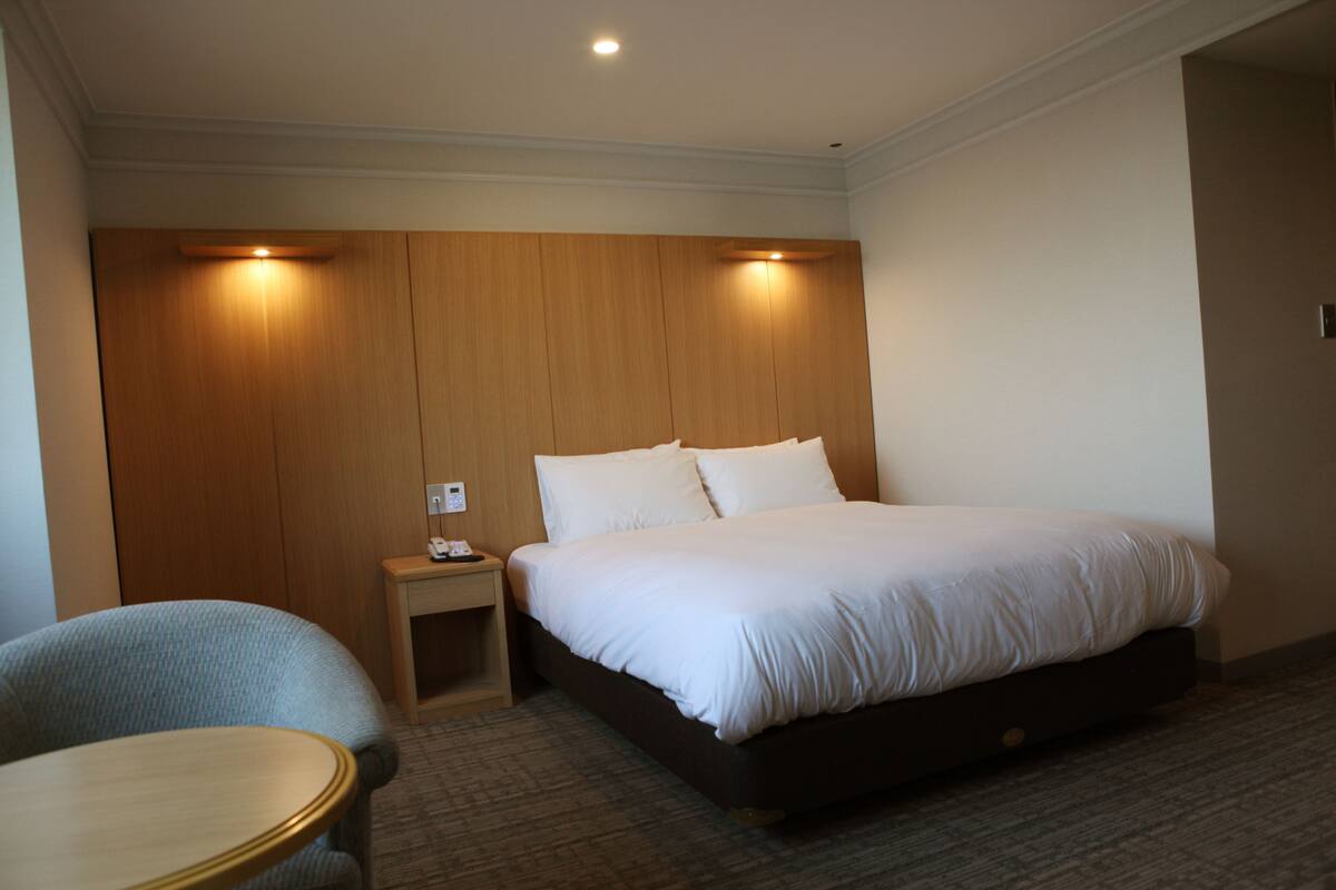 A hotel room with a bed, a bedside table, a chair, and a small table.