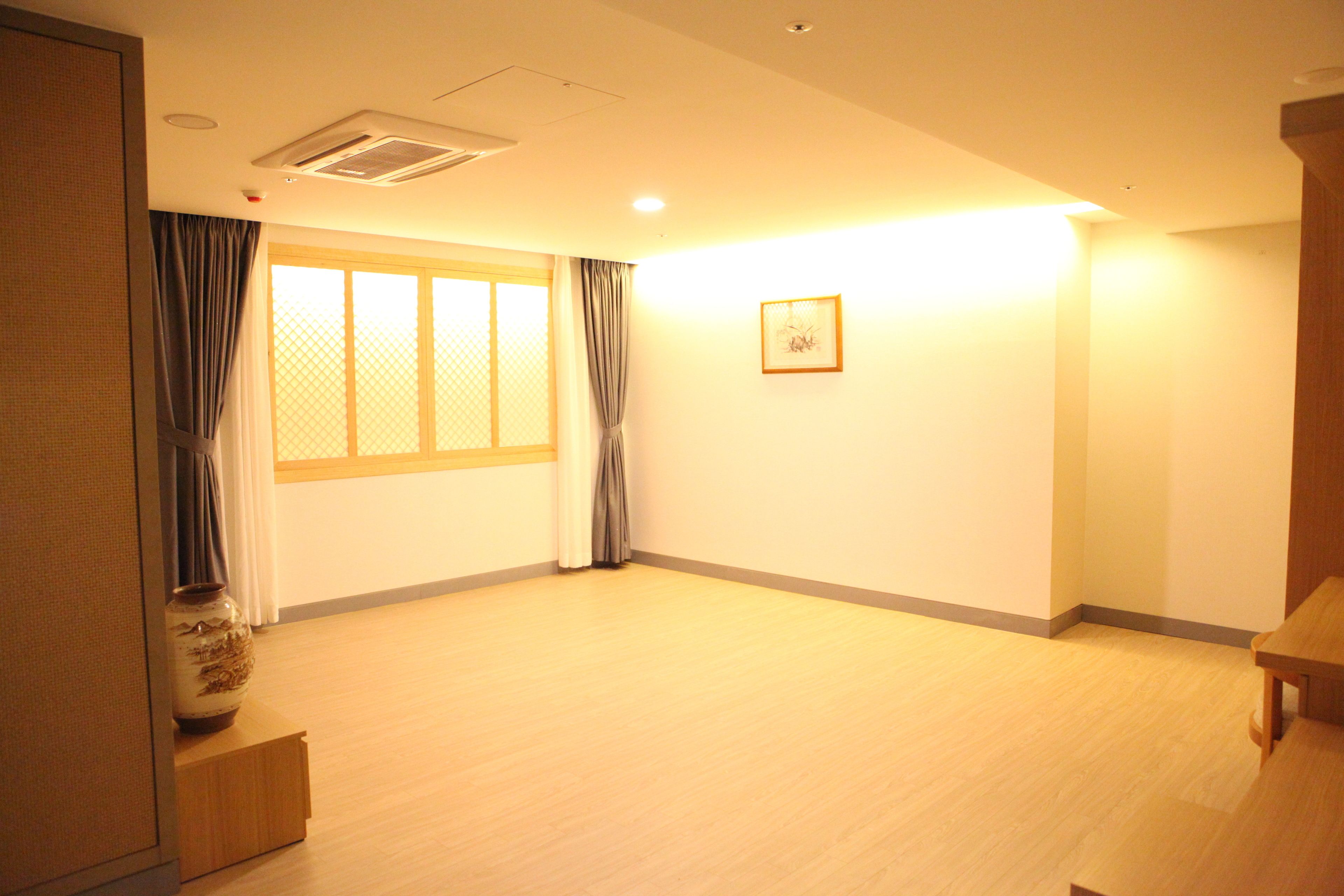 A spacious room with a large window, a framed picture on the wall, and a wooden table.