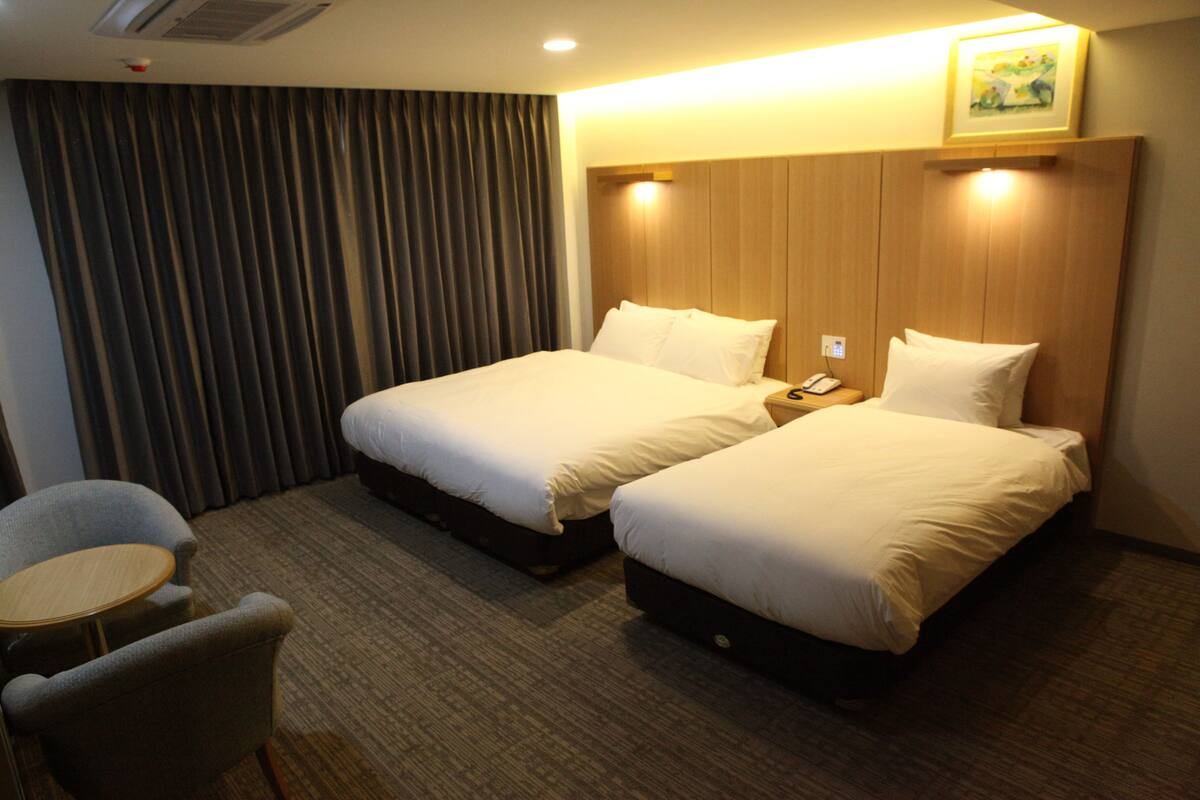 A hotel room with two beds, a small table, and a chair.