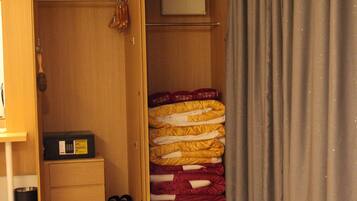 A bedroom with a wooden wardrobe, a bed with a red and yellow blanket, and grey curtains.