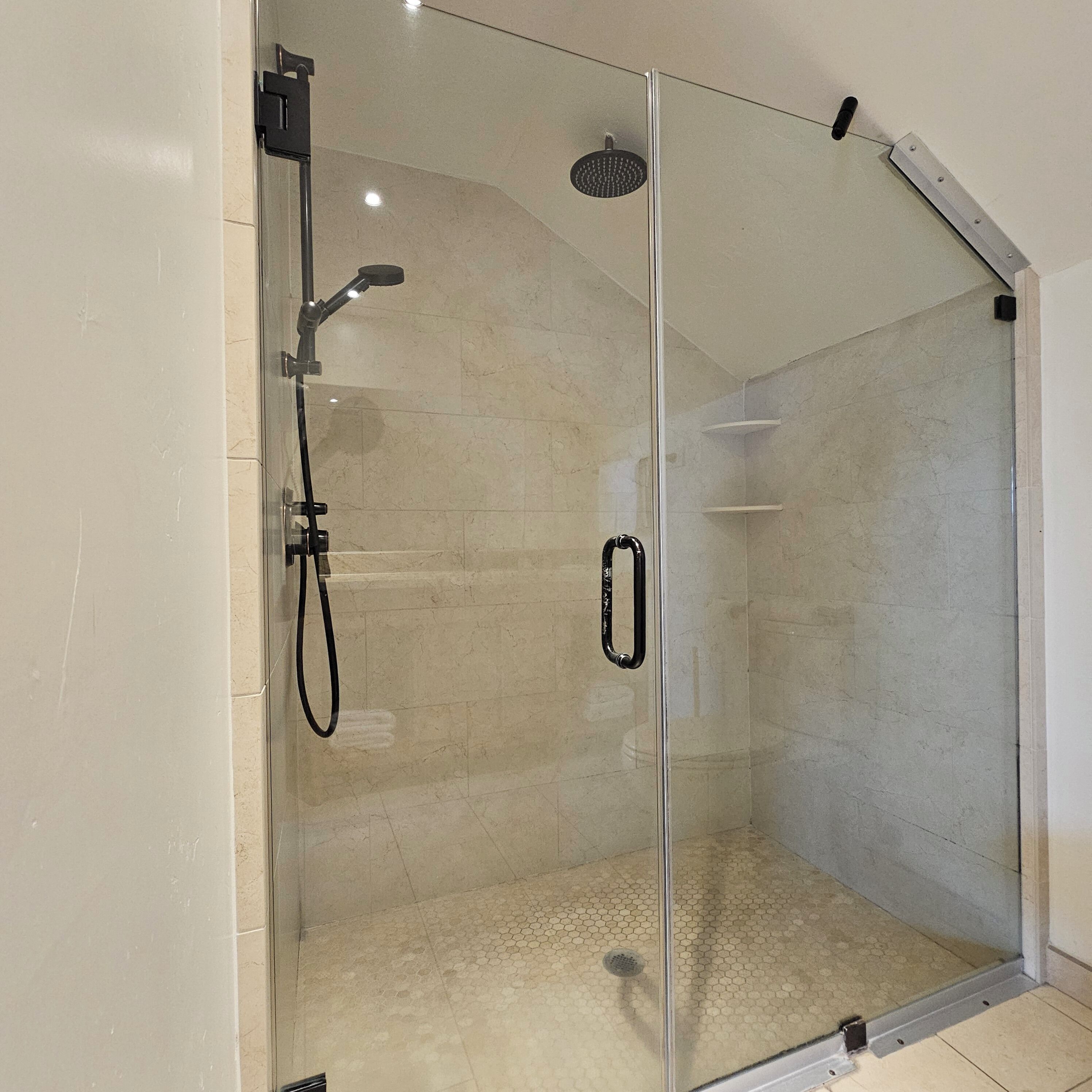 Une douche fermée par des parois en verre, dotée d’un pommeau de douche à main et d’un robinet mural.