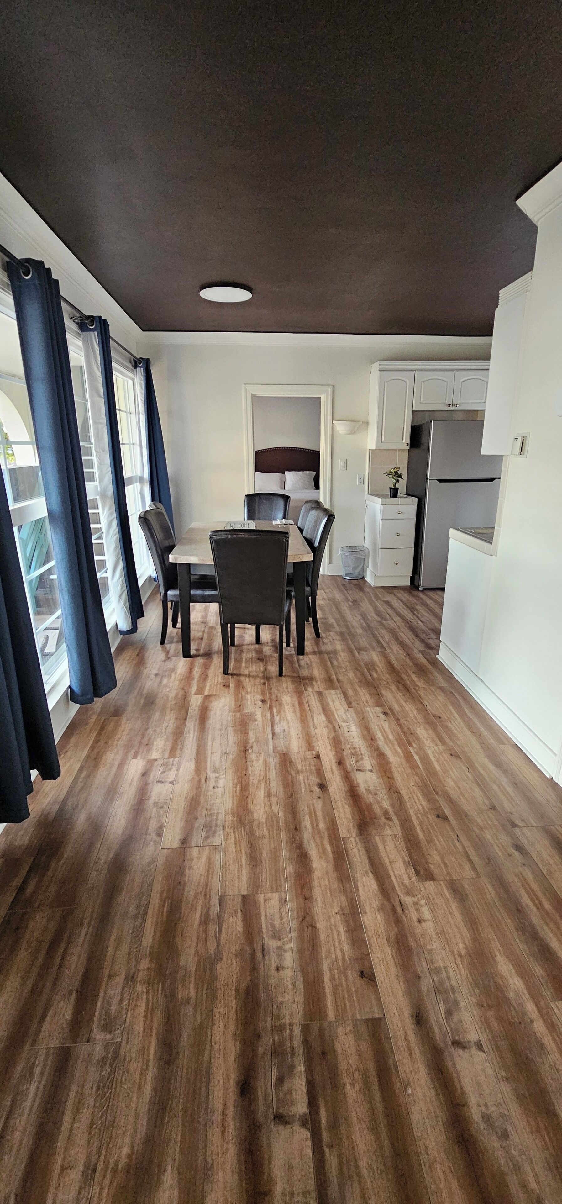 A compact living space with a dining area, kitchenette, and a view through a window with curtains.
