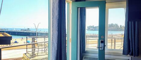 A room with a large window overlooking a beach, a door with a handle, and a wall-mounted air conditioning unit.