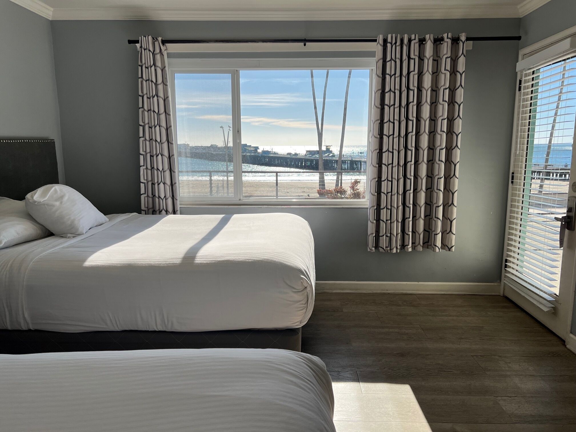 Quarto com duas camas, uma janela grande com cortinas e vista para a praia.