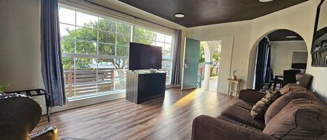 A living room with a large window, a flat-screen TV, a brown sofa, and a wooden floor.