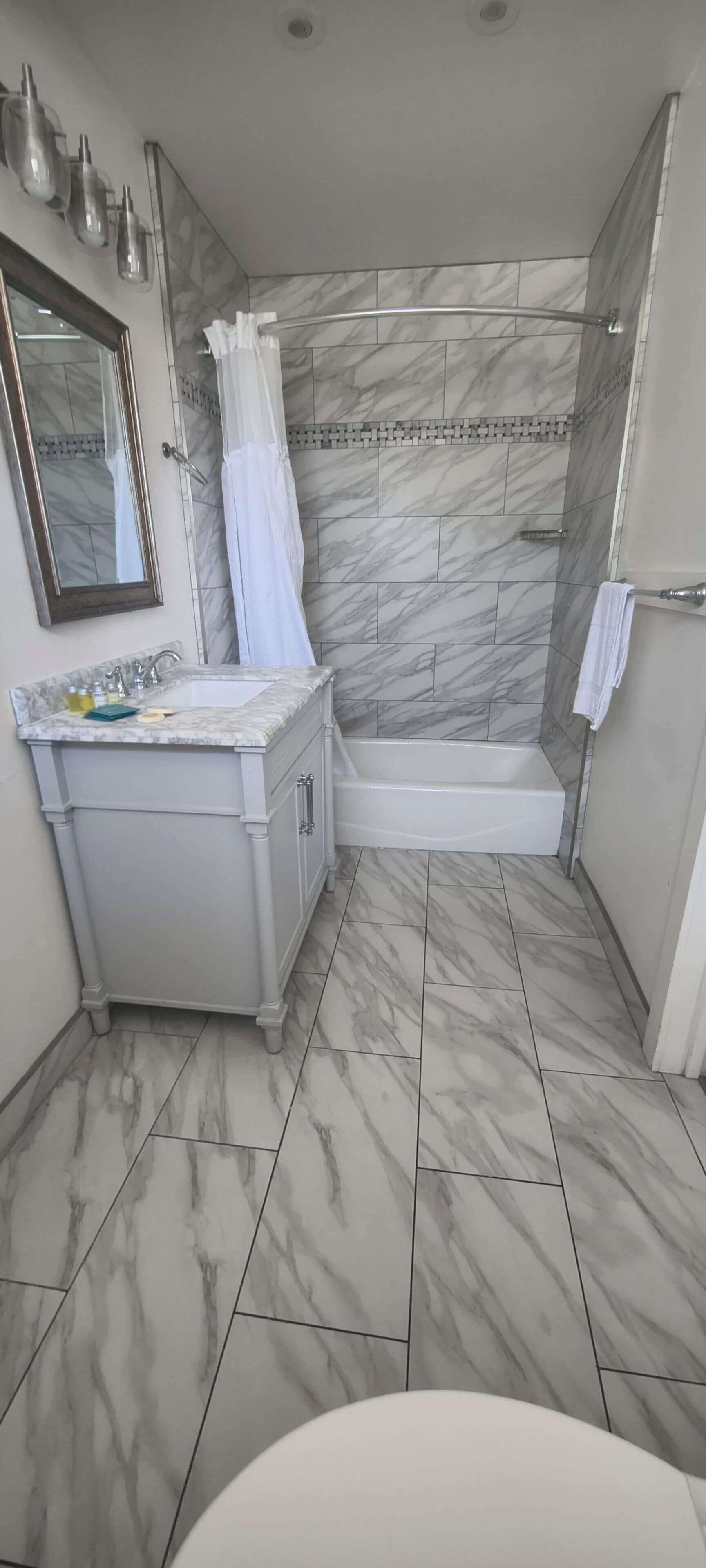 Un baño con piso de mármol, un lavamanos con espejo, una ducha con cortina y una bañera.
