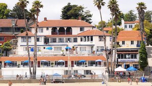 Un hotel frente a la playa con varios balcones, sombrillas de playa y una zona de arena.