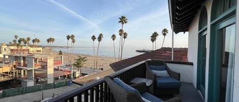 A balcony with wicker furniture overlooking a beach with palm trees and a construction site in the background.
