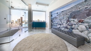 A modern interior with a large stone wall mural, a blue reception desk, and a glass partition. - Olympic Suites Hotel Apartments (Rethymno)