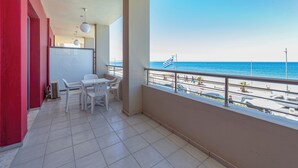 A balcony with a view of the sea, a table with chairs, and a red wall. - Olympic Suites Hotel Apartments (Rethymno)