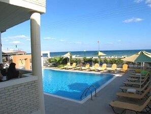 A pool area with lounge chairs and umbrellas, a clear view of the ocean, and a brick wall.
