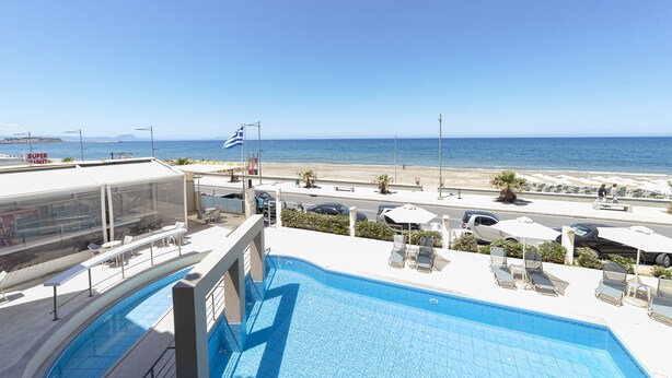 A pool area with lounge chairs and a view of the beach. - Olympic Suites Hotel Apartments (Rethymno)