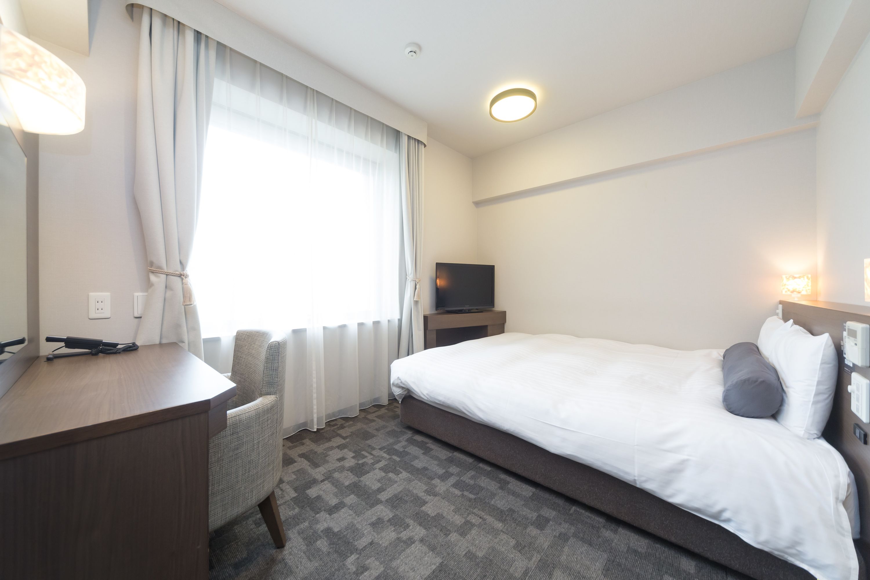 A hotel room with a bed, a desk, a chair, a television, and a window with curtains.