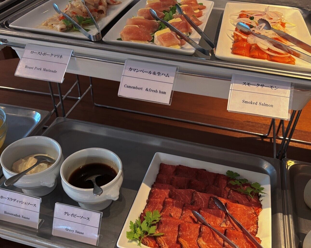A buffet with labeled dishes including roast pork, camembert, smoked salmon, horseradish sauce, and gravy sauce.