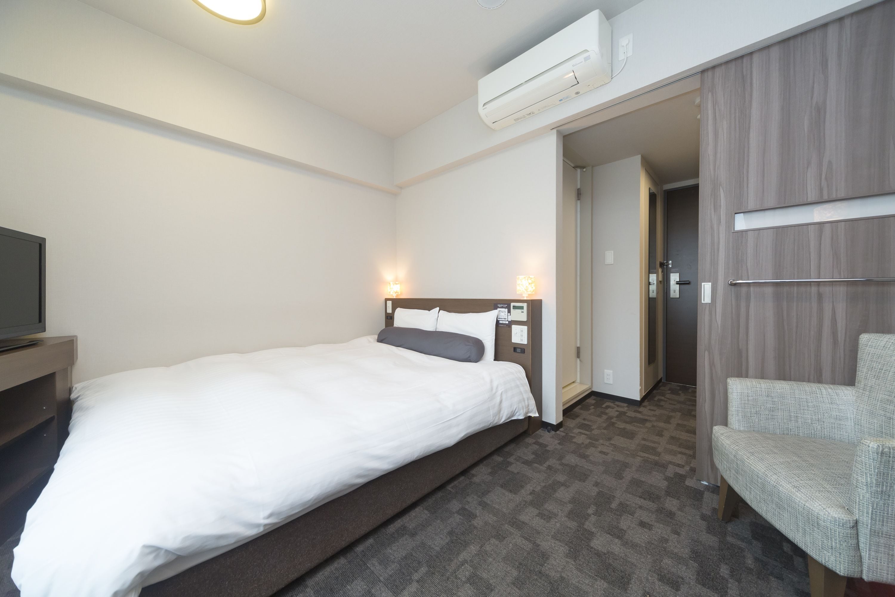 Una habitación de hotel con cama, televisor, silla y armario.