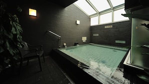 An indoor swimming pool with a skylight, dark brick walls, and a bench. - Dormy Inn Premium Shibuya Jingumae Hot Spring (Tokyo)