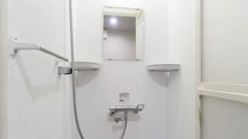 Un petit espace de douche fermé, de couleur blanche, équipé d’un pommeau de douche à main, d’un miroir fixé au mur et d’un panneau de commande.