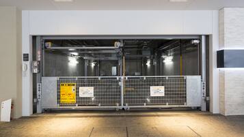An elevator with metal gates and warning signs, a fire extinguisher, and a vented ceiling.
