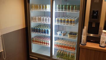 Un refrigerador de bebidas repleto de diversas opciones, incluyendo latas y botellas, y un dispensador de agua a la derecha.