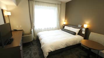 Une chambre d’hôtel comprenant un lit, un bureau avec une télévision, une chaise, une petite table et une fenêtre avec des rideaux.