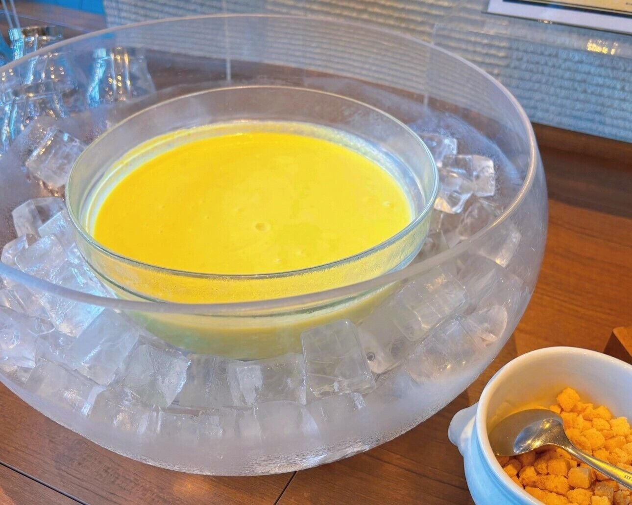 Een schaal gele vloeistof op een ijsblokjesvorm, een lepel, en een schaal met croutons.