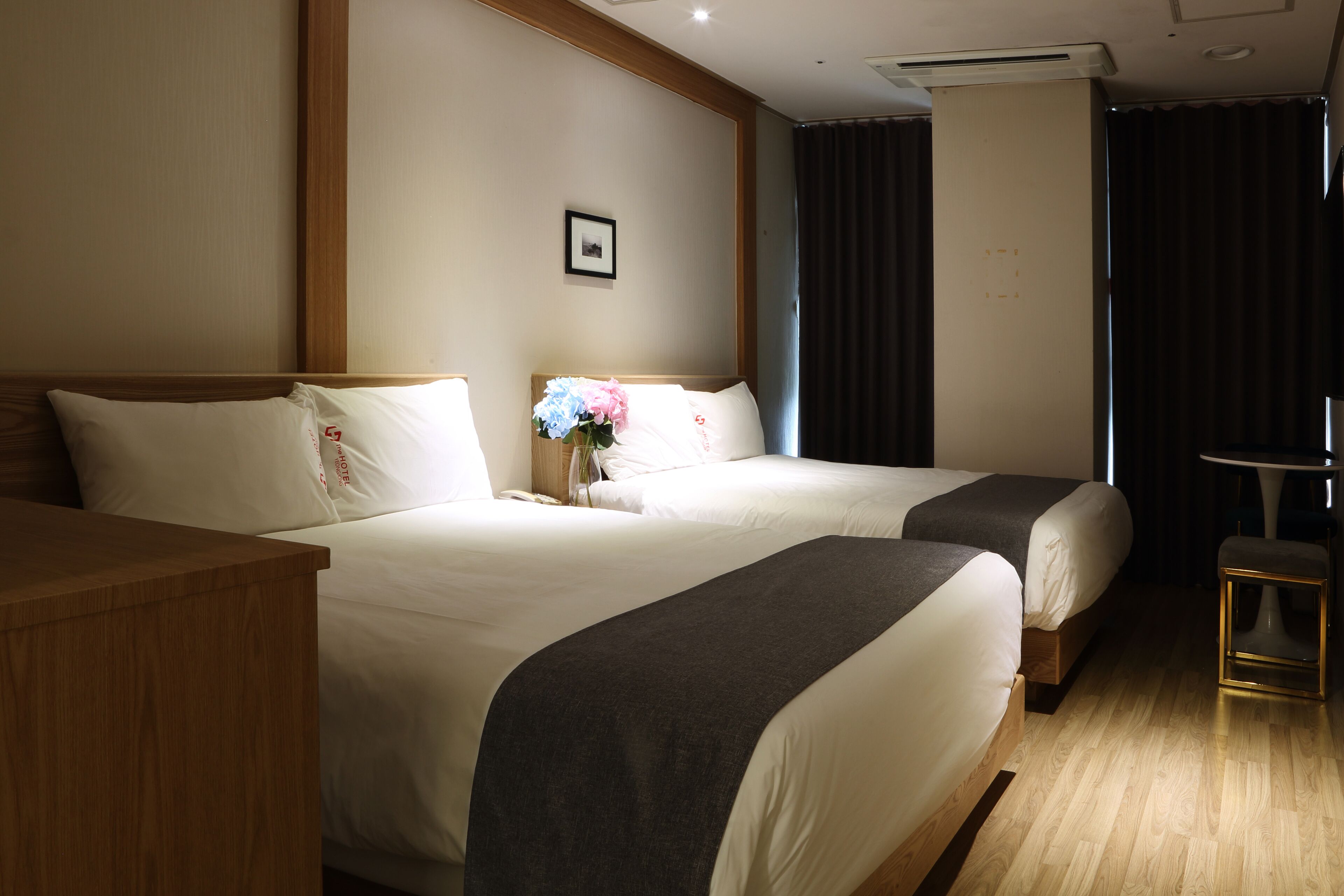 A hotel room with two beds, a wooden nightstand, a small table, and a picture on the wall.