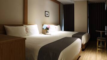 A hotel room with two beds, a wooden nightstand, a small table, and a picture on the wall.