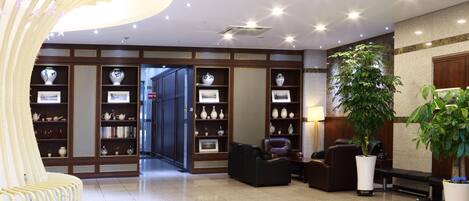 A lobby with a reception desk, seating area, and a wall with shelves displaying vases.