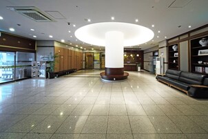 A spacious lobby with a central column, a reception desk, a seating area, and a bookshelf.
