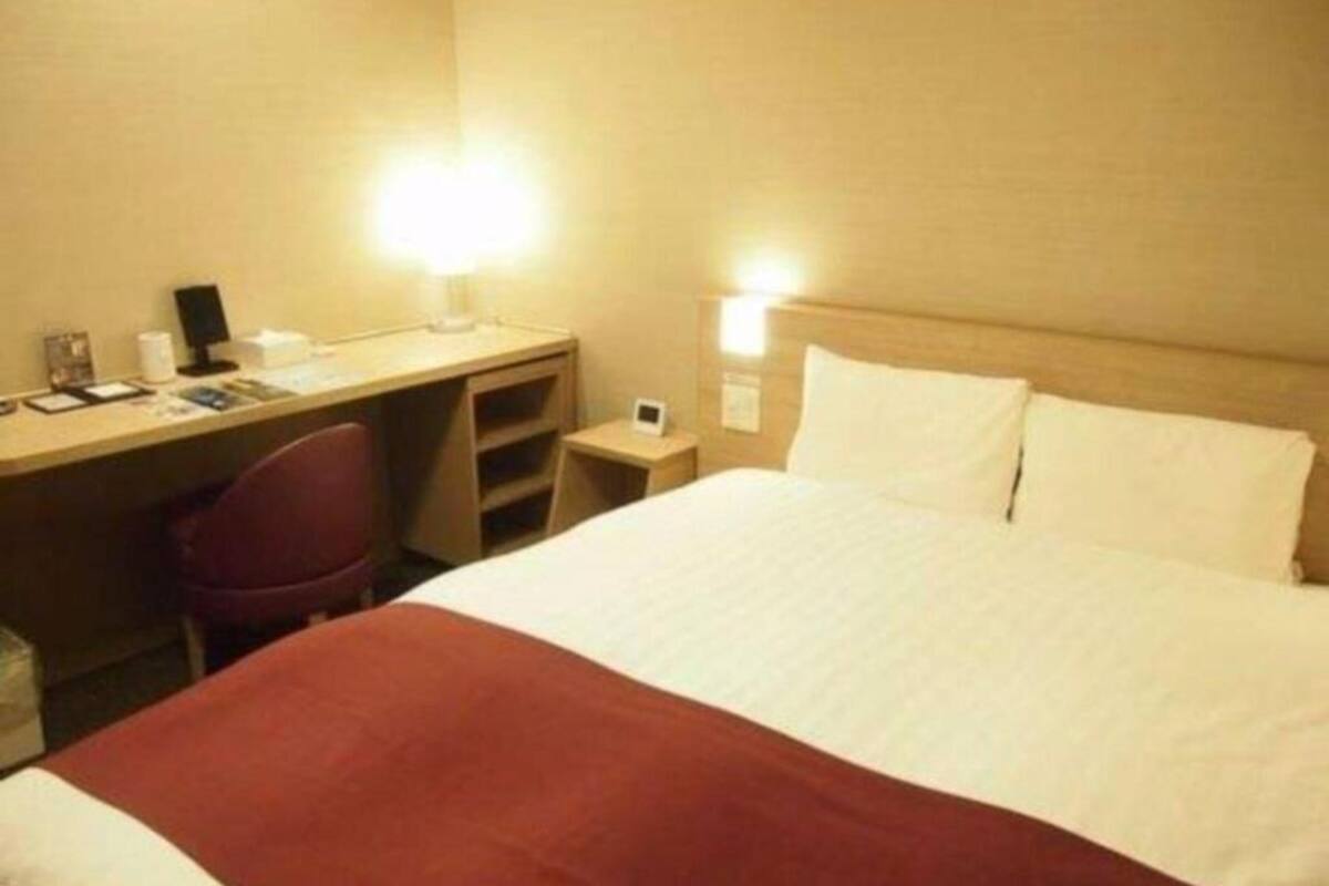 A hotel room with a bed, desk, chair, and bedside table.