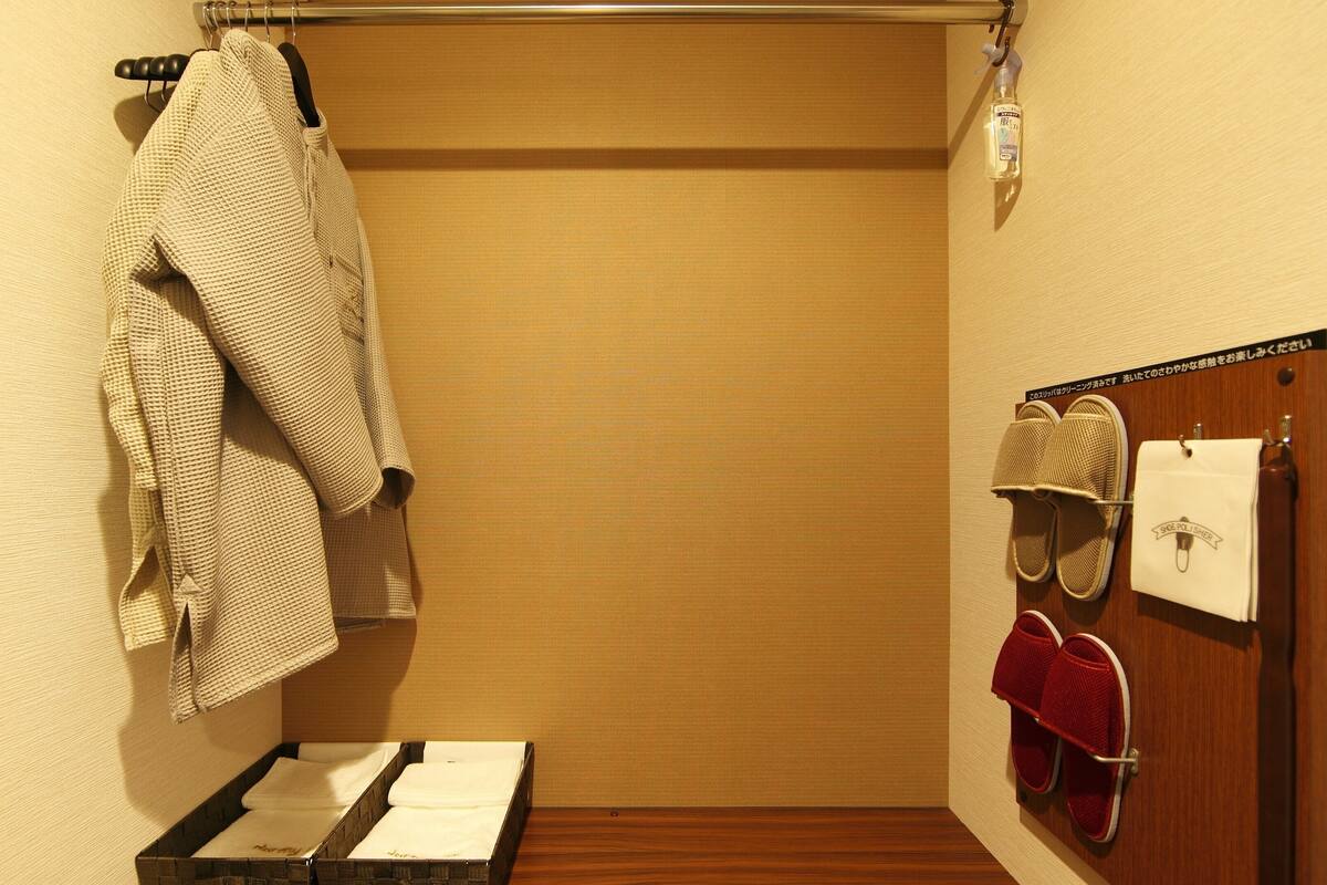 A small, narrow bathroom with a towel rack, a shoe rack, and a bottle of hand sanitizer.