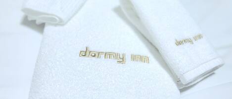 Una toalla blanca doblada con el texto 'dormy inn' bordado en dorado.