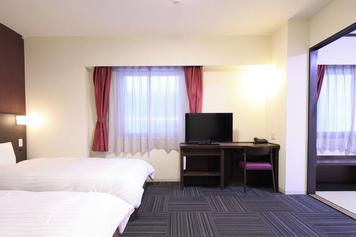 A hotel room with a bed, a desk with a television, and a chair.